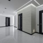 Modern spacious corridor with white walls and floor and black doors and ceiling decorated with LED lights